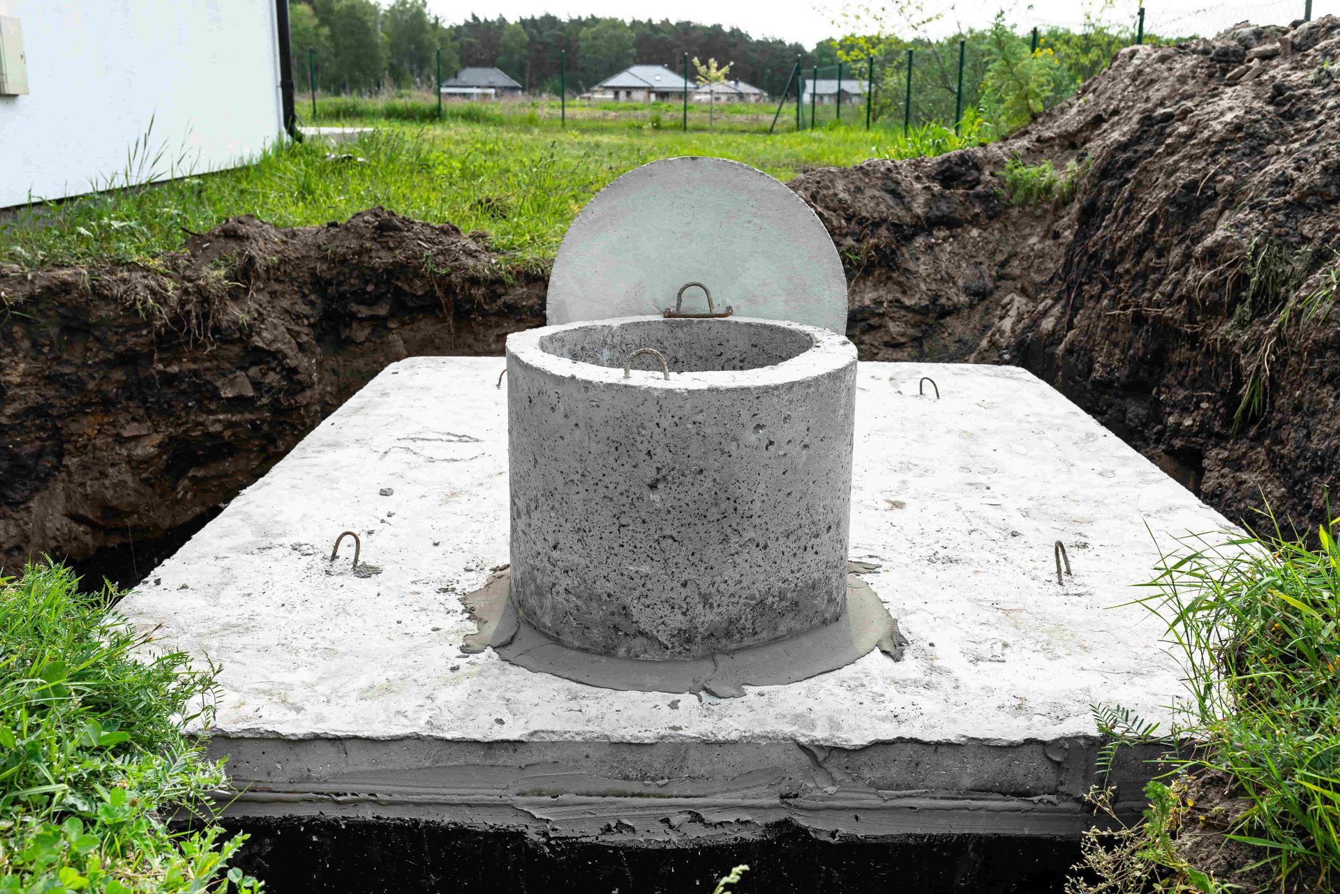 Concrete septic tank in a partially dug pit, with a lid and access opening.
