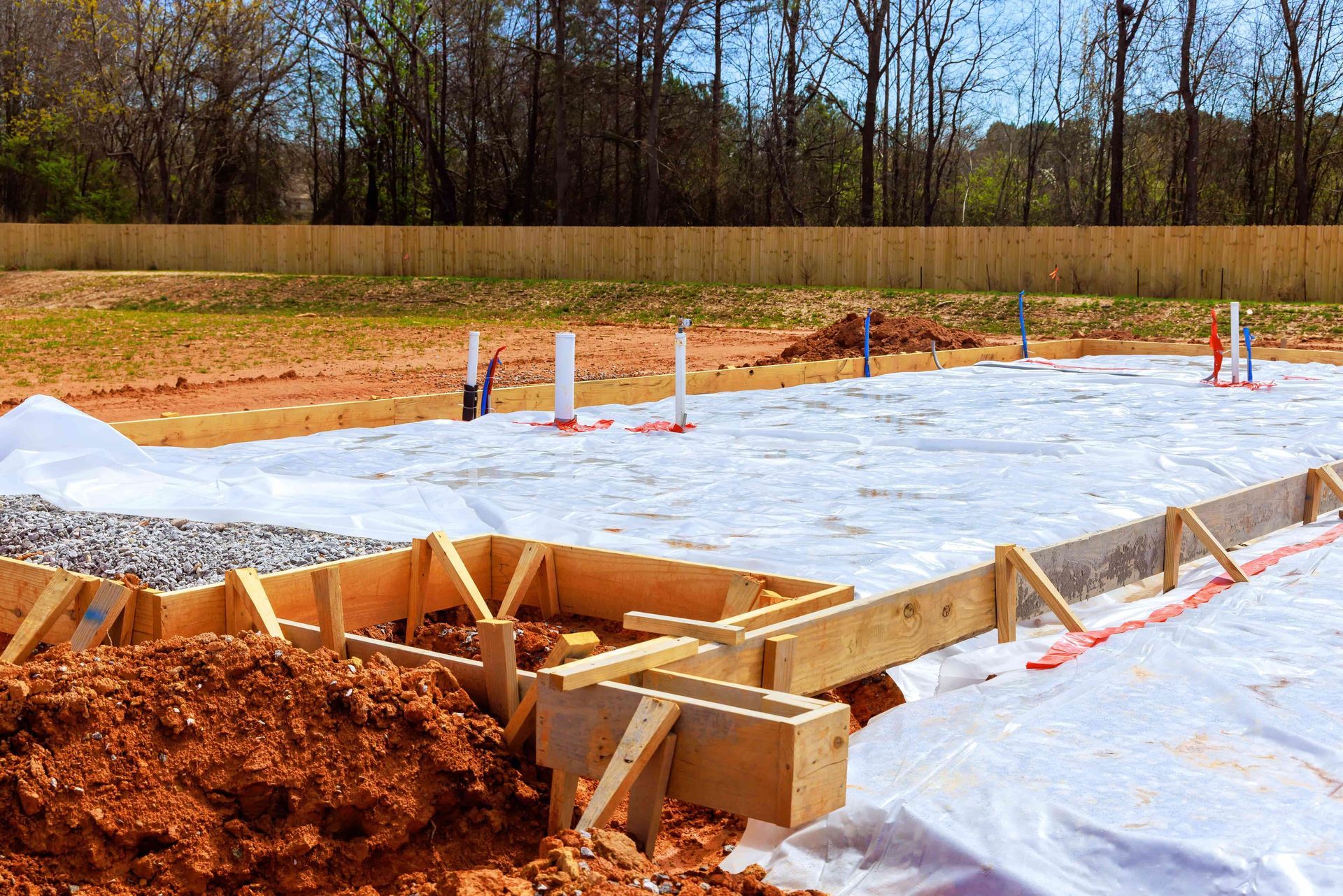 Foundation of a building under construction, wooden forms, white sheeting, plumbing, dirt.