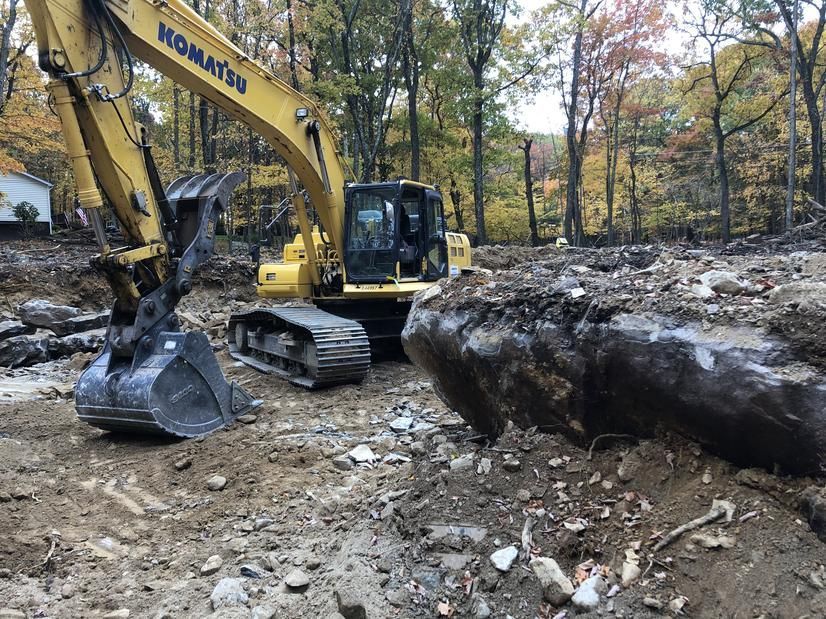 Yellow Komatsu excavator digging in a dirt area, logs and trees in the background.