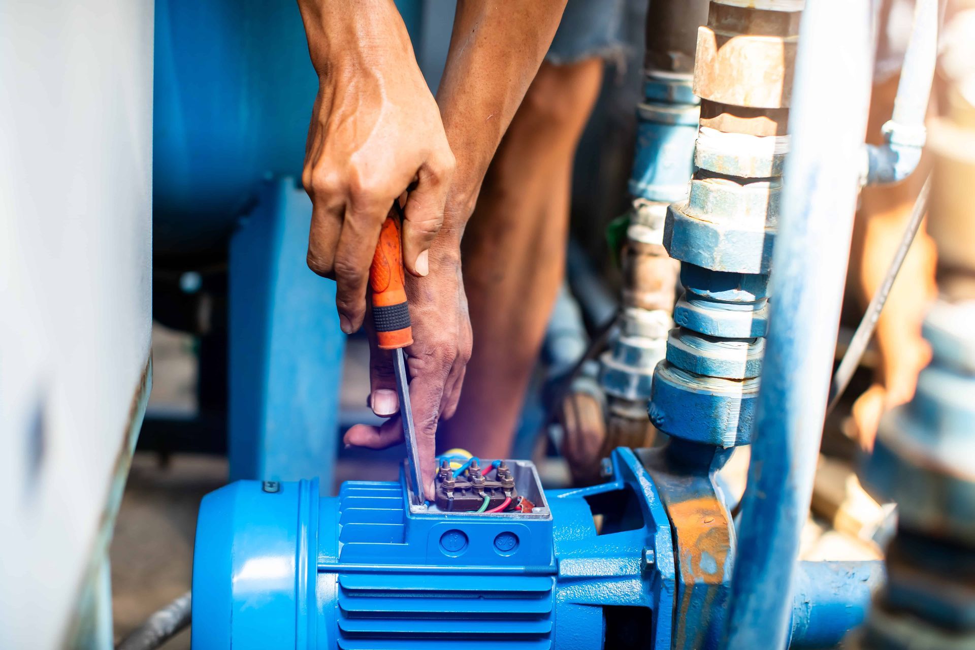 Person repairs a blue water pump with a screwdriver, outdoors.