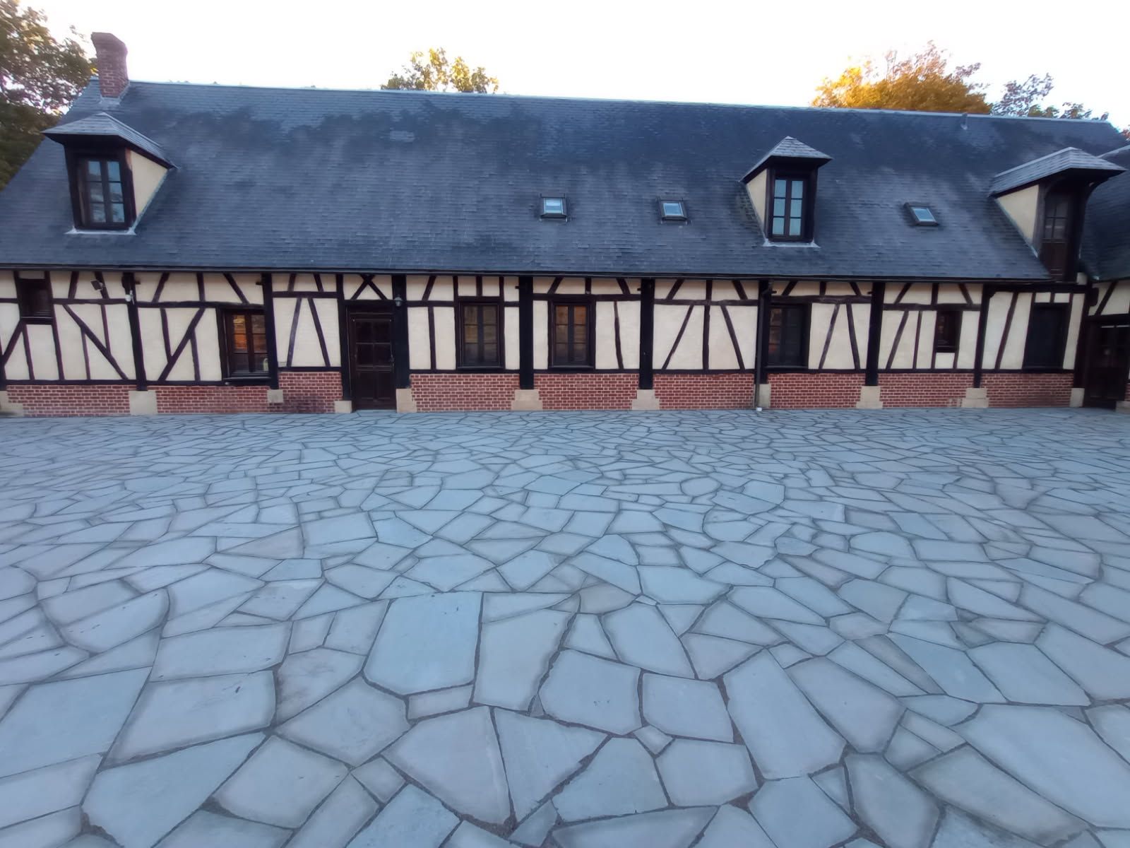 A courtyard with a stone floor and a timber-framed building with a dark roof.