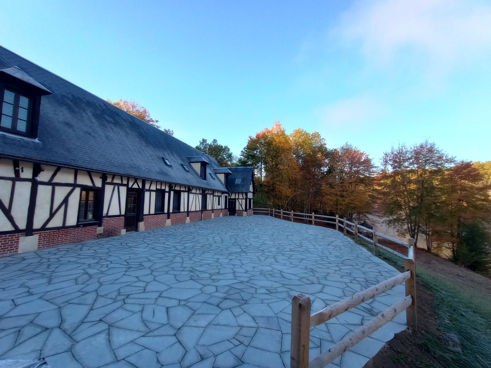 A long, half-timbered building with a stone patio and wooden fence on a sunny day.