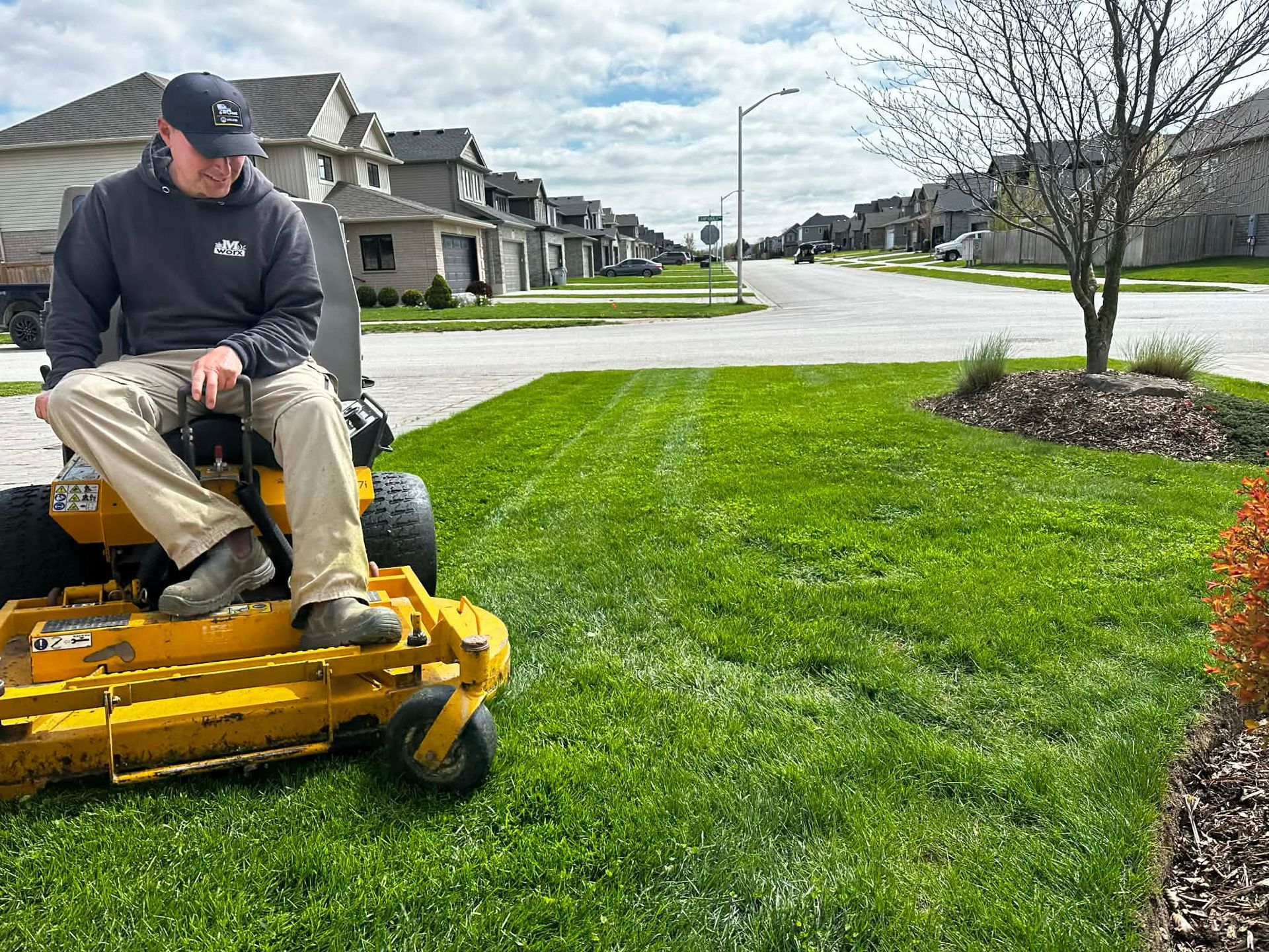 Man riding a yellow mower on a suburban lawn beside a row of houses on a sunny day