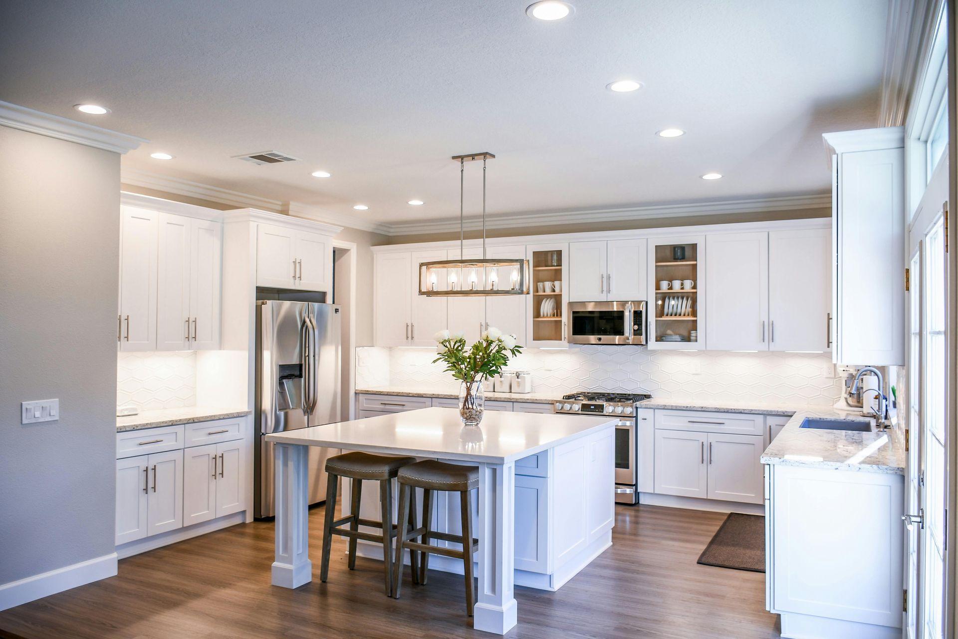 White kitchen with island, stainless steel appliances, and wooden flooring.