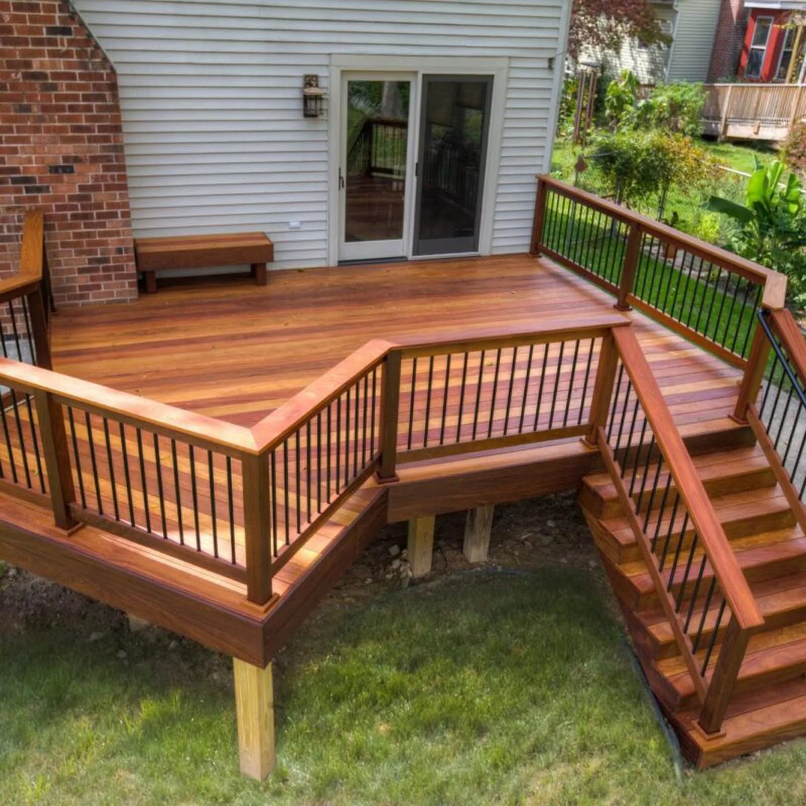 Raised wooden deck with stairs, railing, and bench beside a house door
