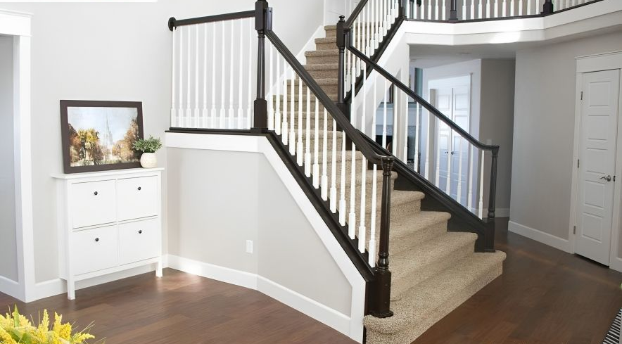 A staircase with carpeted steps and a white and black railing inside a light gray-painted home.