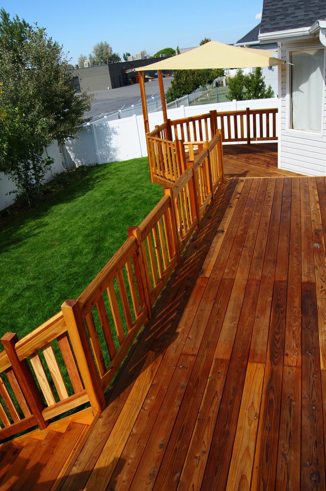 Wooden deck with a railing next to green lawn. A shade sail covers a raised platform.