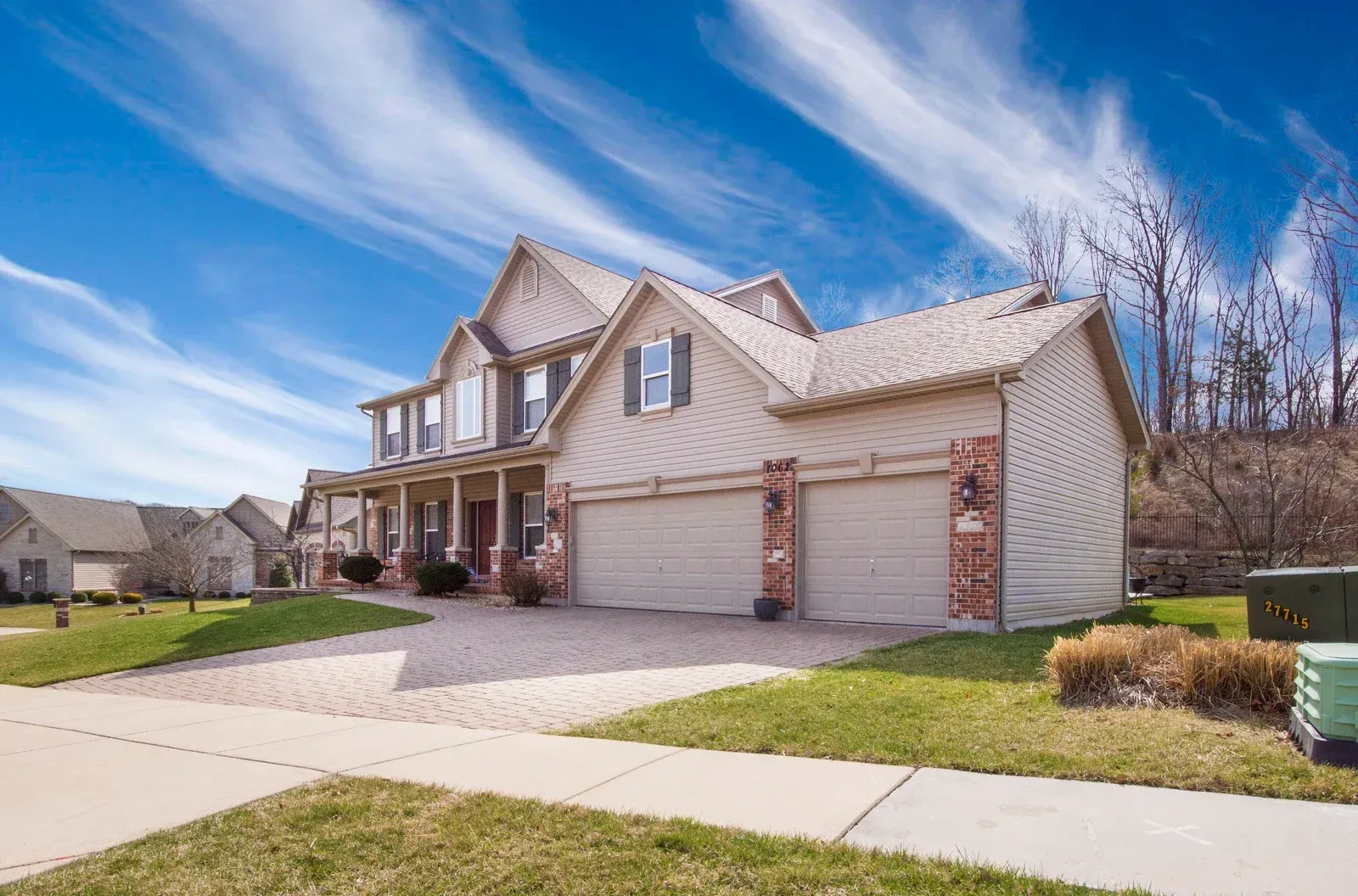 Two-story beige house with a two-car garage under a blue sky with streaky clouds.