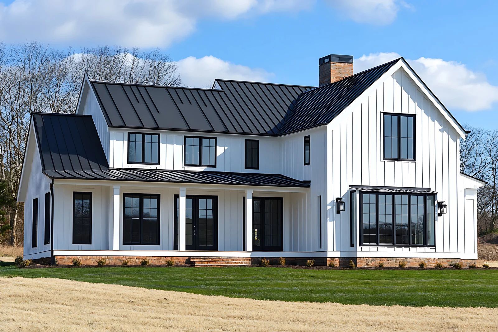 White farmhouse with black roof, windows, and trim, on green grass under blue sky.