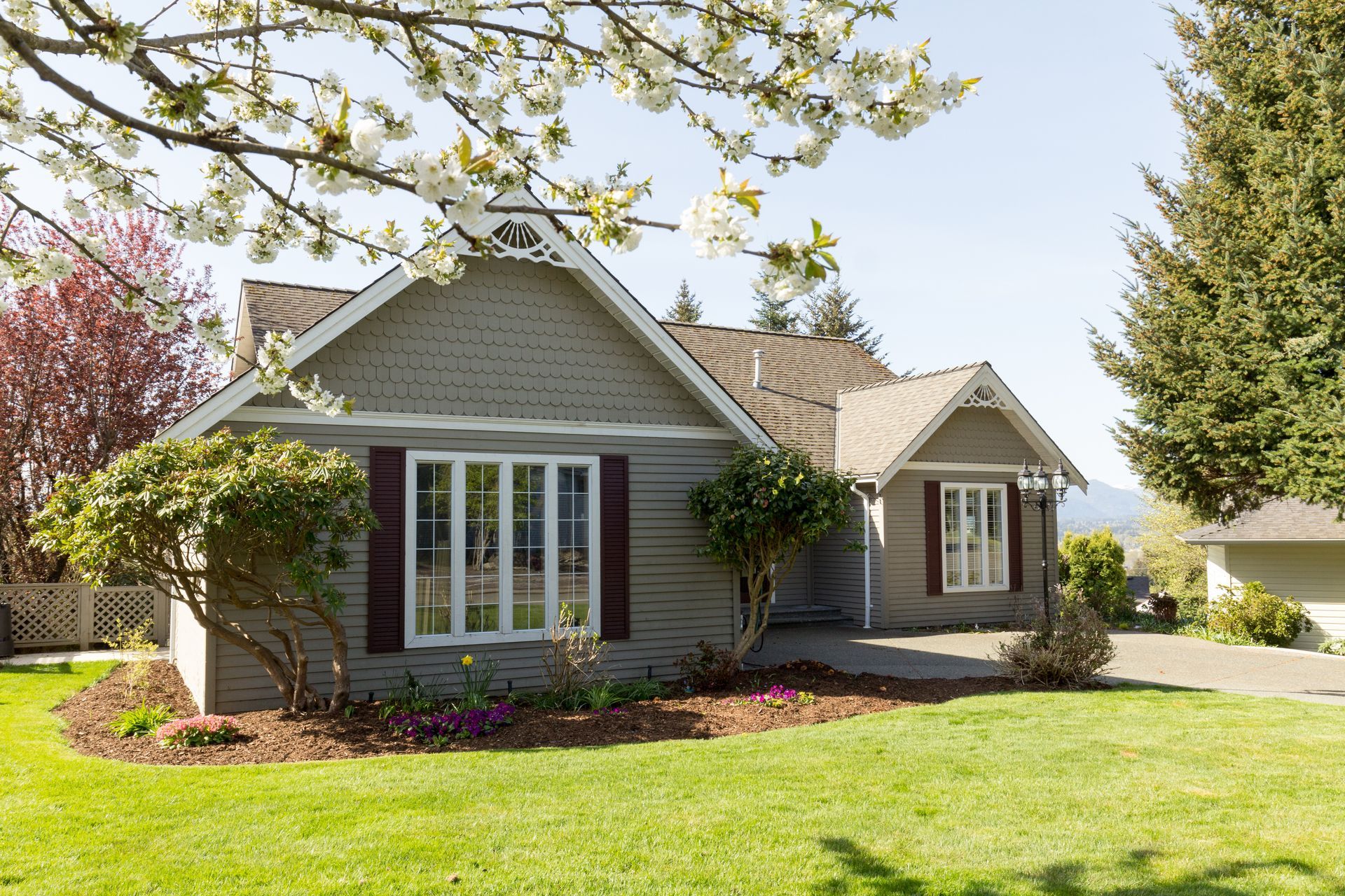 Gray house with white trim and a front lawn, framed by trees and spring blossoms