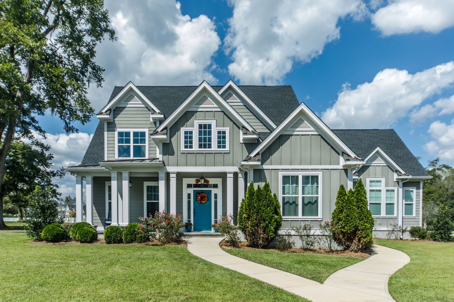 Two-story gray house with a blue front door, white trim, and a curved walkway under a bright sky