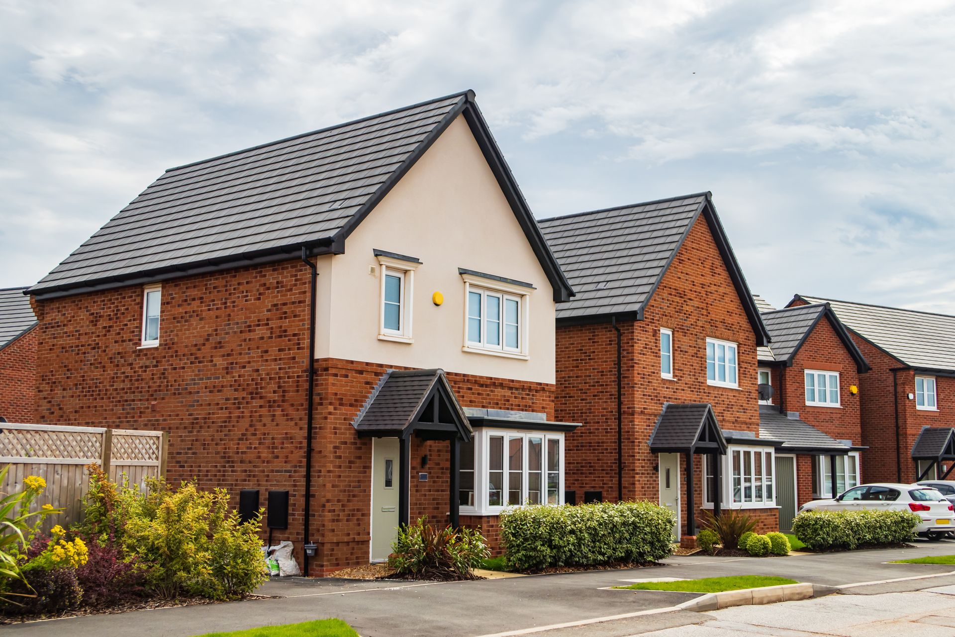 Row of modern brick townhouses with cream facades and parked cars on a suburban street