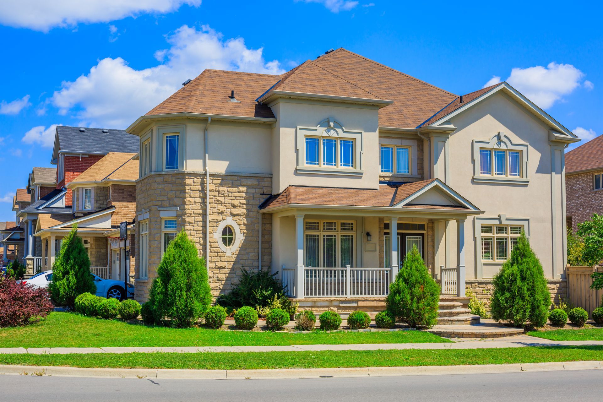 Large two-story suburban house with stone accents, red roof, and a manicured green lawn