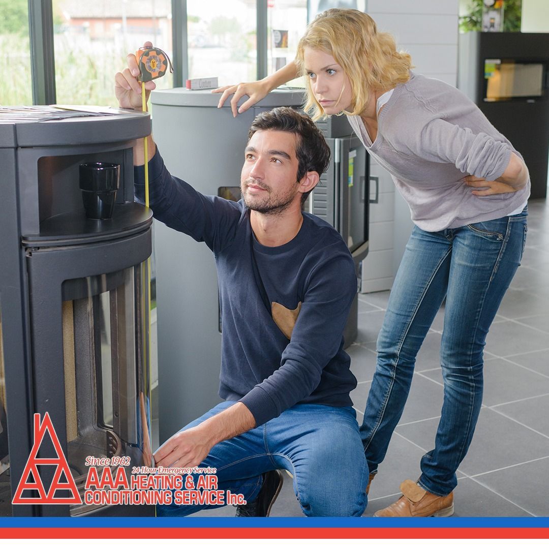 Man installing a wood stove with a woman observing. Indoors, they are focused, man is kneeling and holding tools.