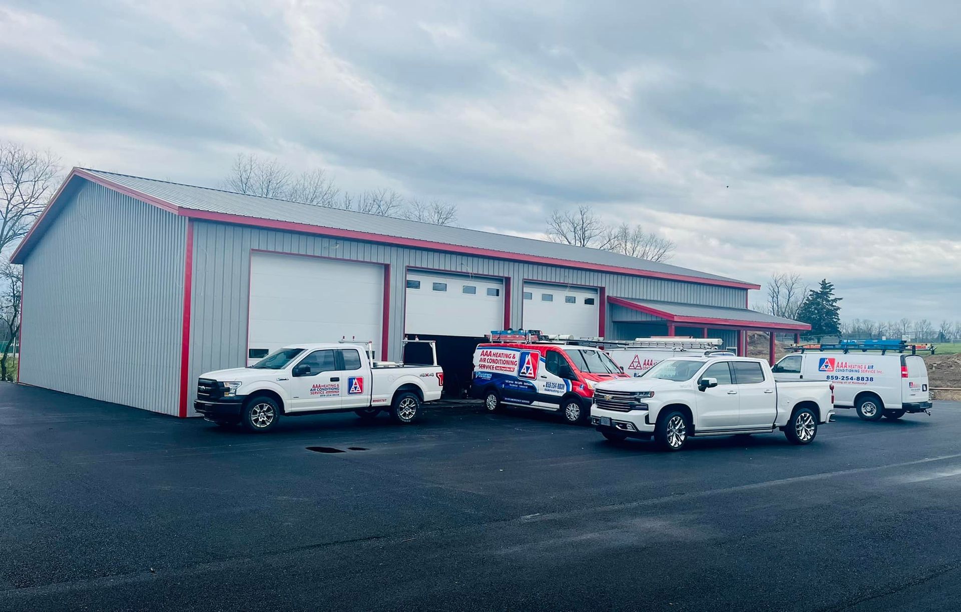 Vehicles with company logos parked in front of a metal building with garage doors.