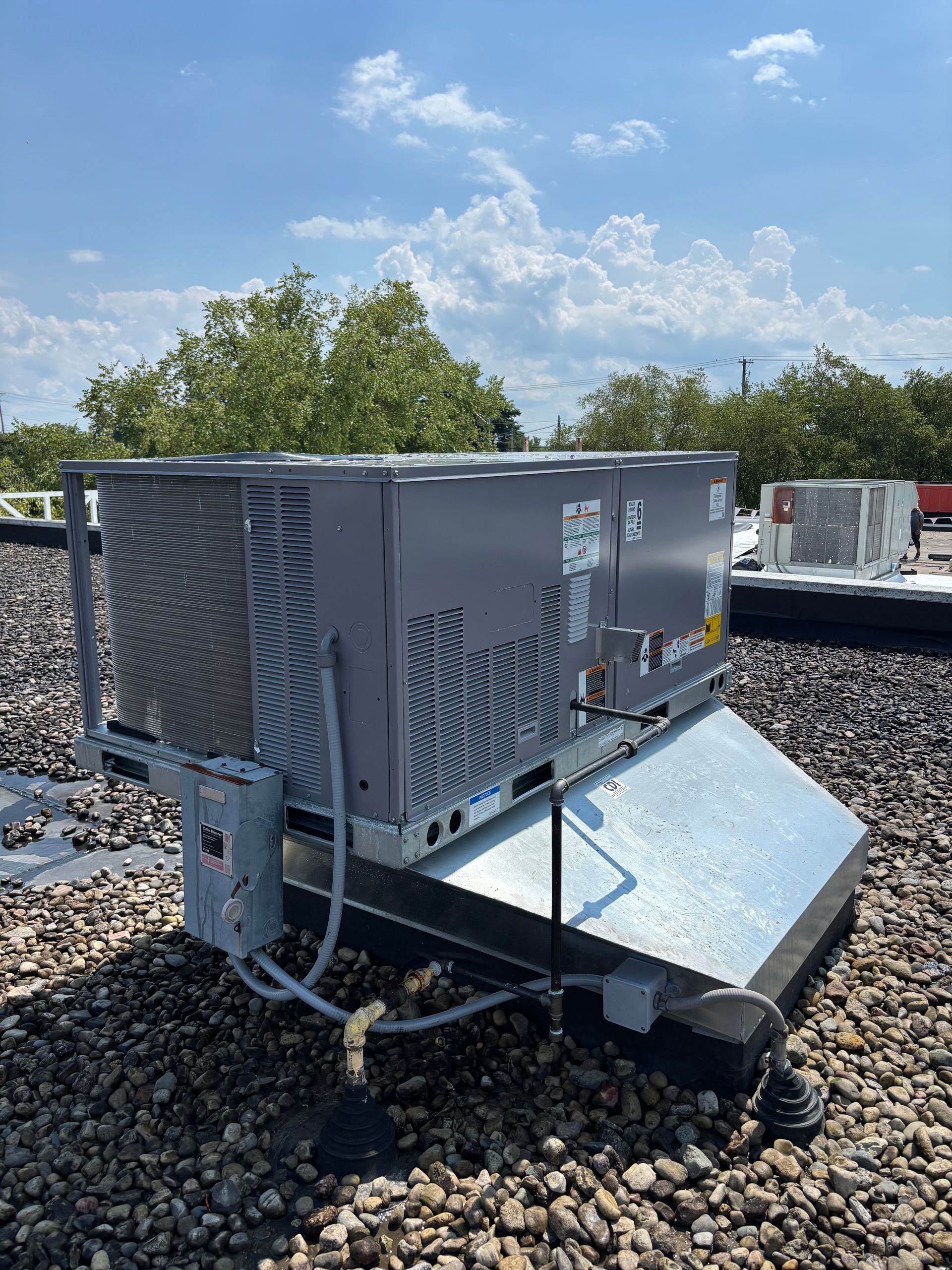 An air conditioning unit on a rooftop with a cloudy sky in the background.