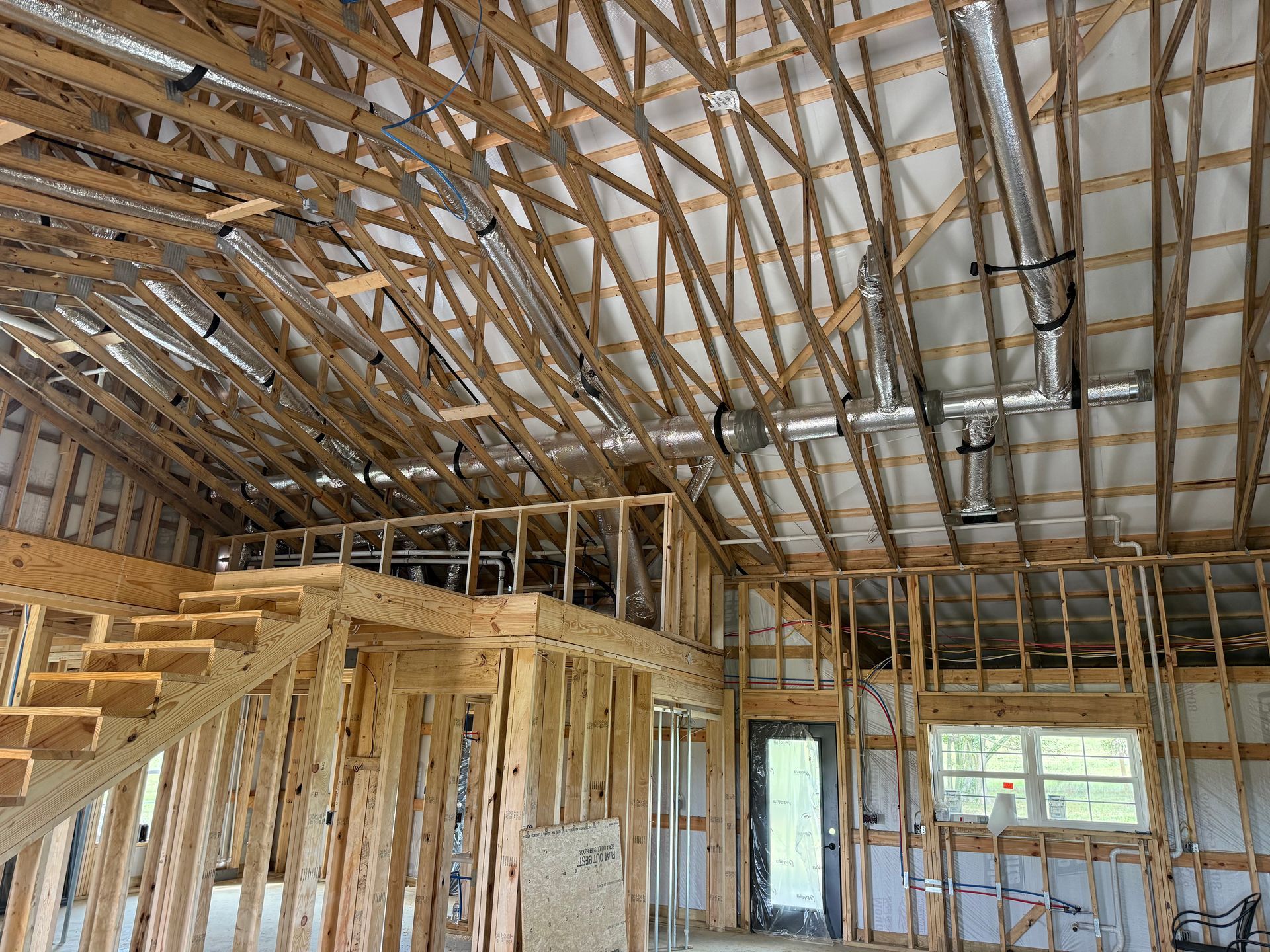 Interior view of a building under construction, showing wooden framing, ductwork, and a staircase.