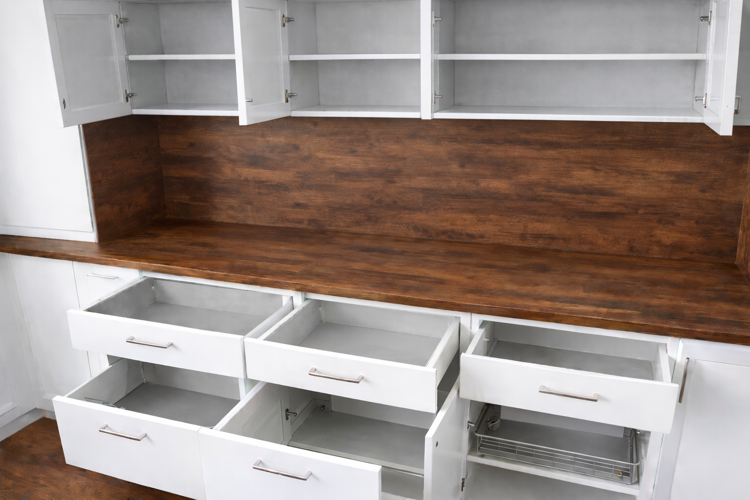 Des armoires de cuisine blanches avec tiroirs ouverts et placards hauts, contrastant avec un plan de travail en bois foncé.