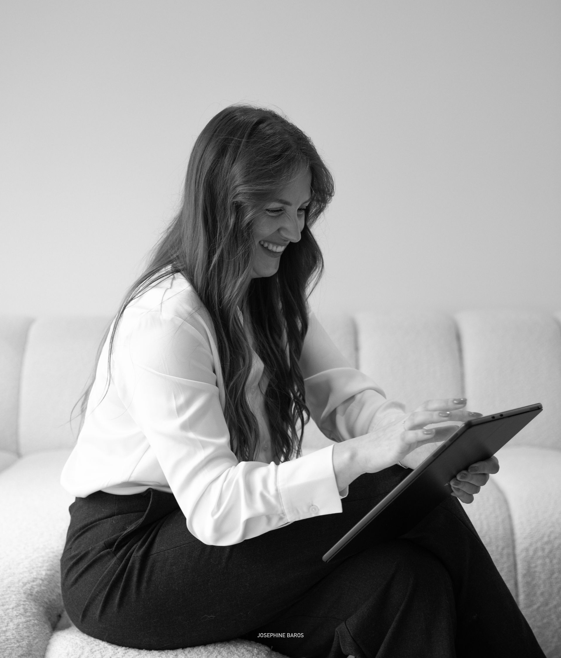 Femme aux longs cheveux bruns, vêtue d'une chemise noire, souriant à l'extérieur devant un bâtiment moderne.
