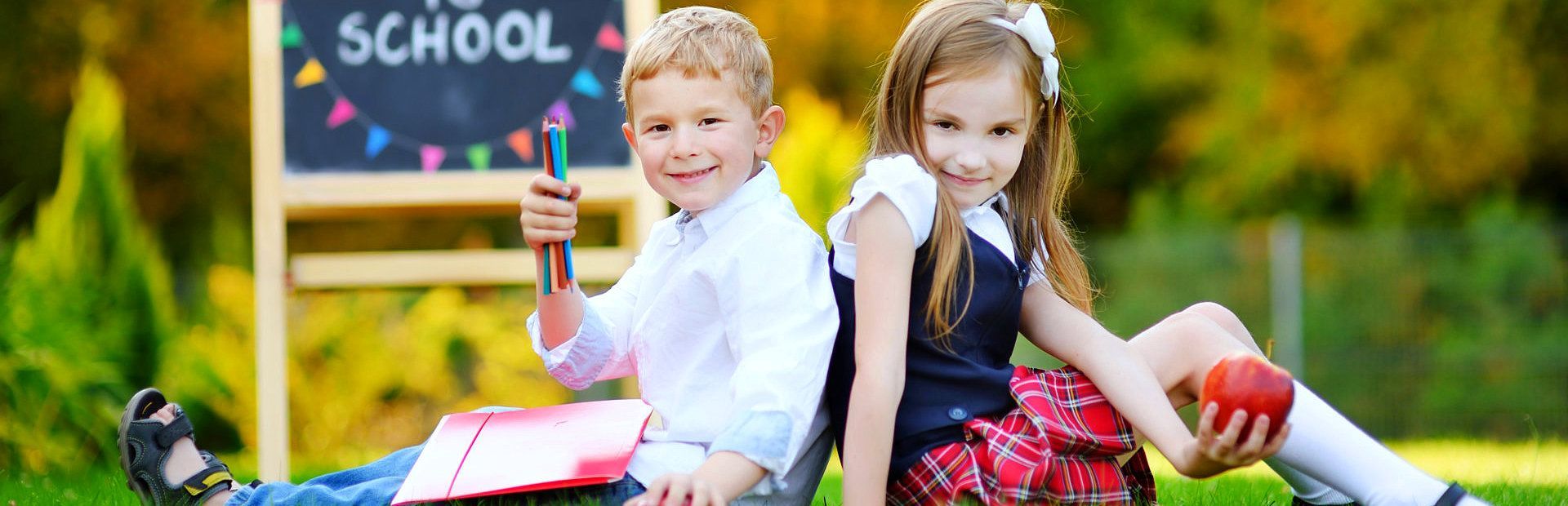 A boy and a girl are sitting back to back in front of a school sign.