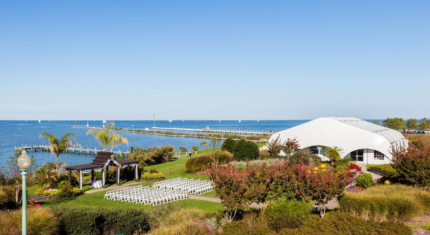 A large white tent is sitting on top of a lush green field next to the ocean.