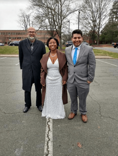 A bride and groom are posing for a picture in a parking lot.