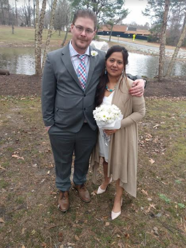 A man in a suit and tie is standing next to a woman holding a bouquet of flowers.