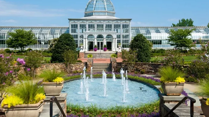 A large greenhouse with a fountain in front of it.