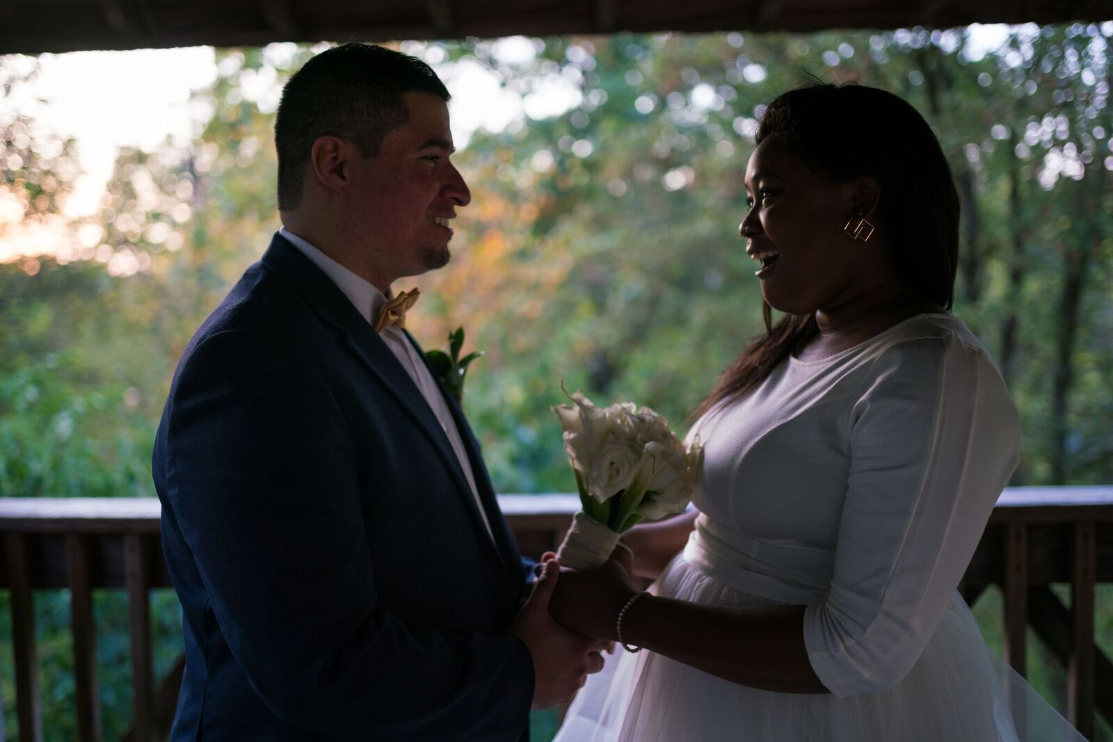 A bride and groom are holding hands and looking at each other on a balcony.