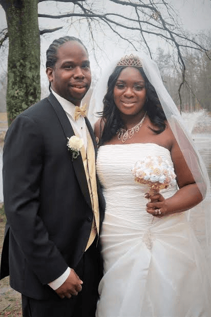 A bride and groom pose for a picture in front of a tree
