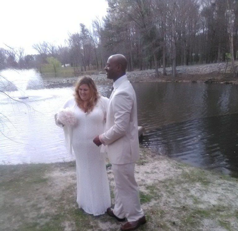 A bride and groom are standing next to a body of water.