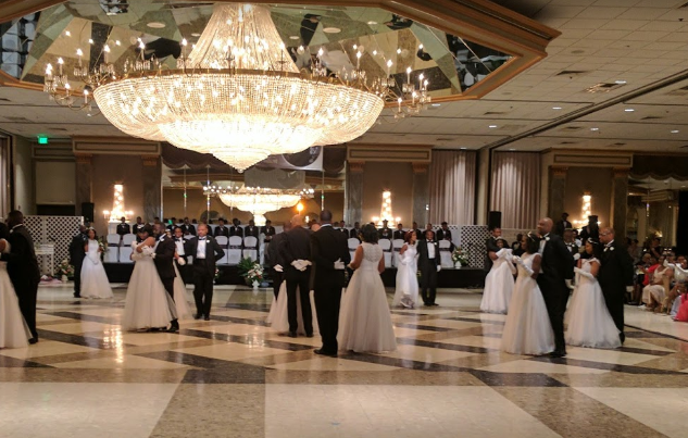 A group of people are dancing in a ballroom under a chandelier.