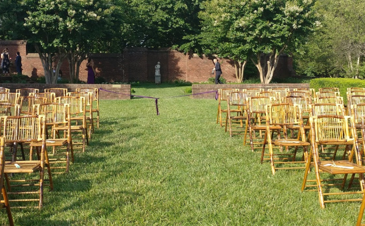 A row of wooden folding chairs are lined up in a grassy field.