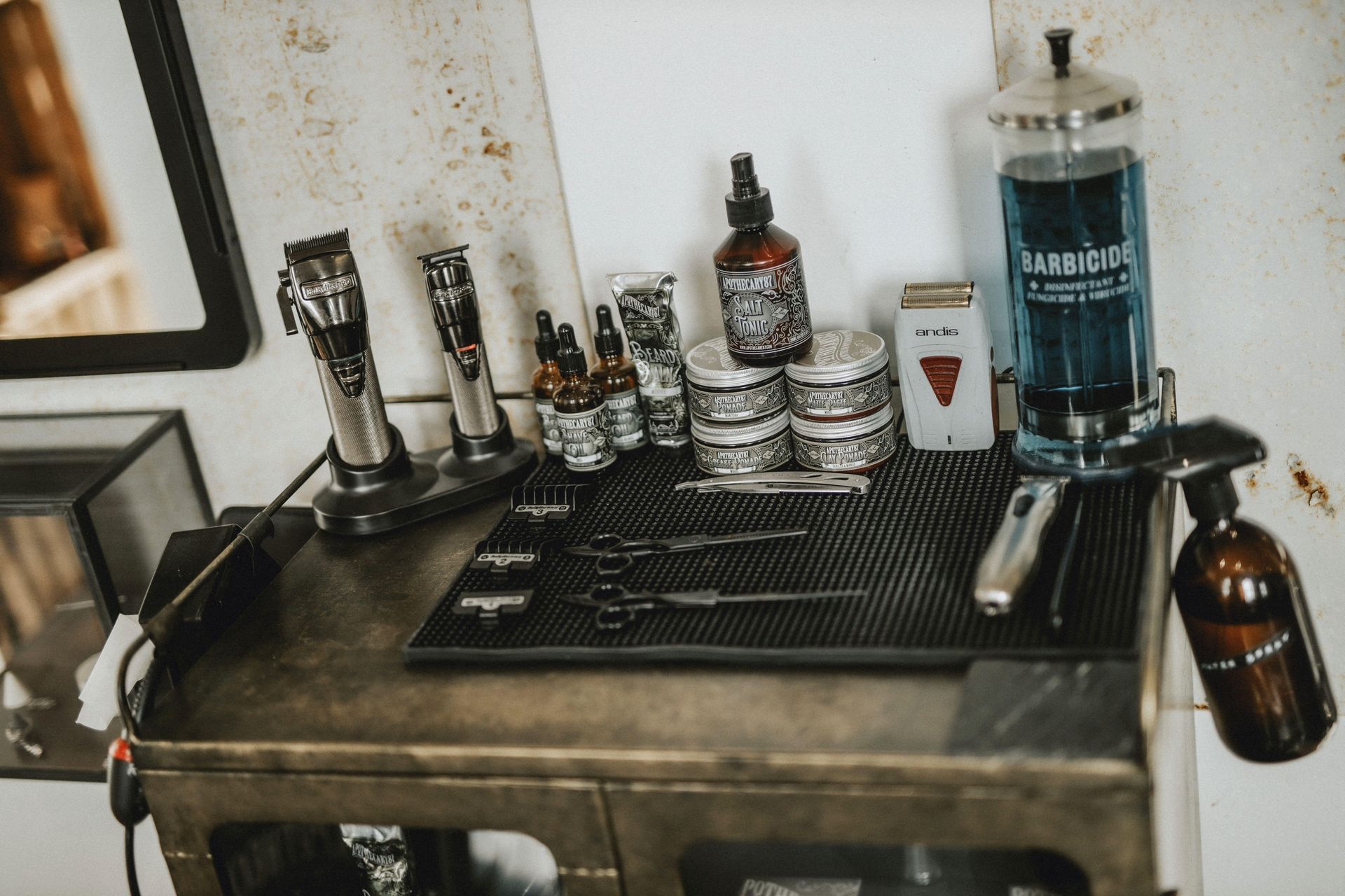 Barber station with clippers, sprays, and grooming tools on a metal counter near a mirror