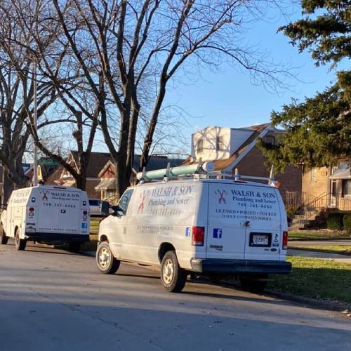 Two white vans are parked on the side of the road