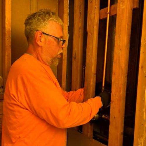 A man in an orange shirt is working on a wooden wall.