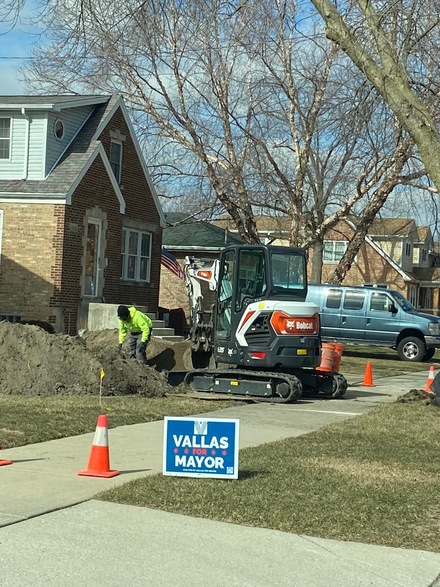 A man is digging a hole in the ground next to a sign that says vallas mayor.