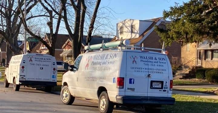 Two white vans are parked on the side of the road in front of a house.