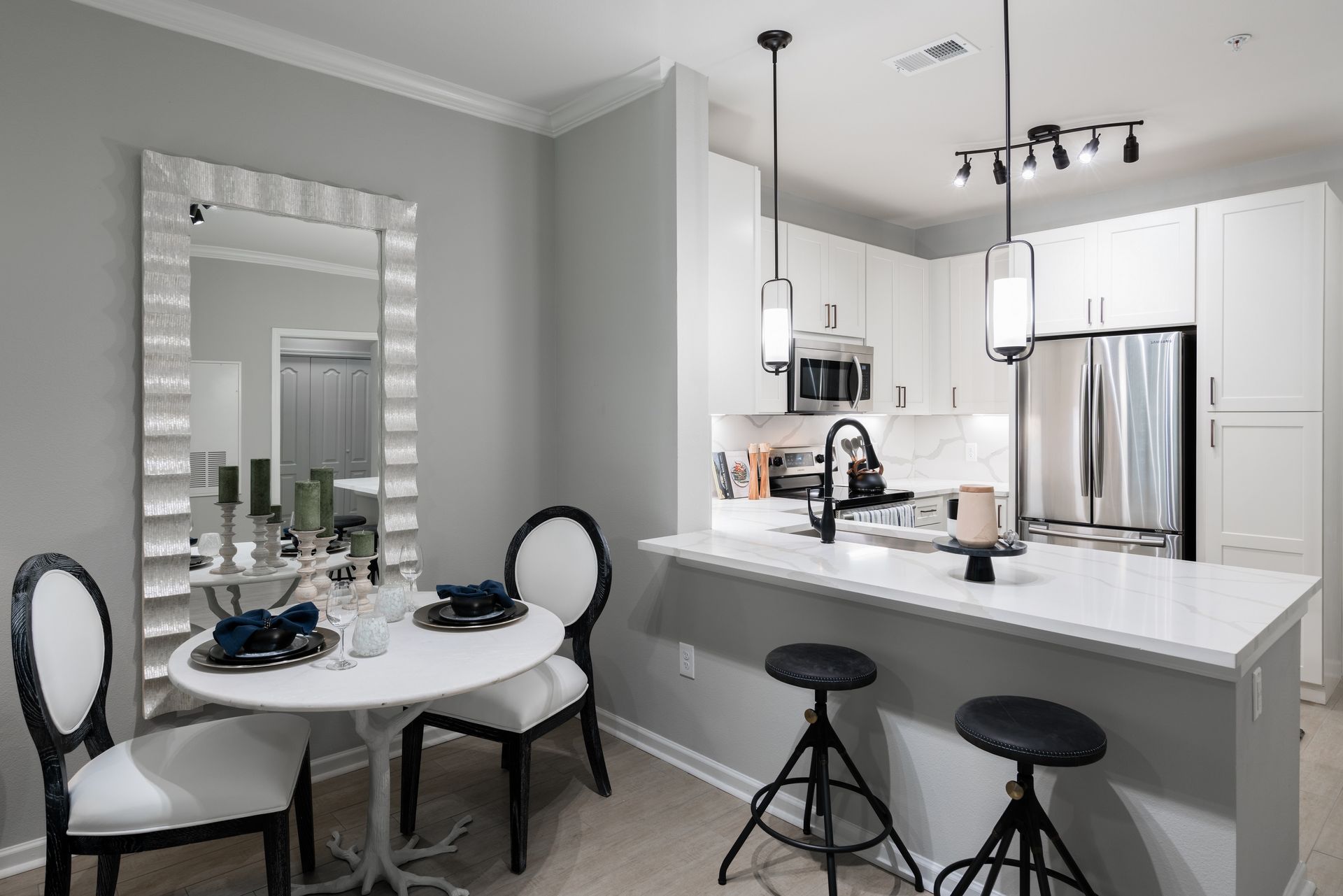 Bright kitchen with white cabinets, island with stools, and a dining table with a mirror.