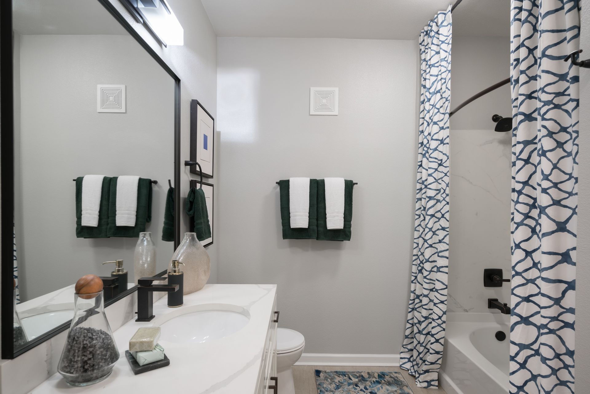 Bathroom with a white countertop, dark fixtures, and teal and white accents.