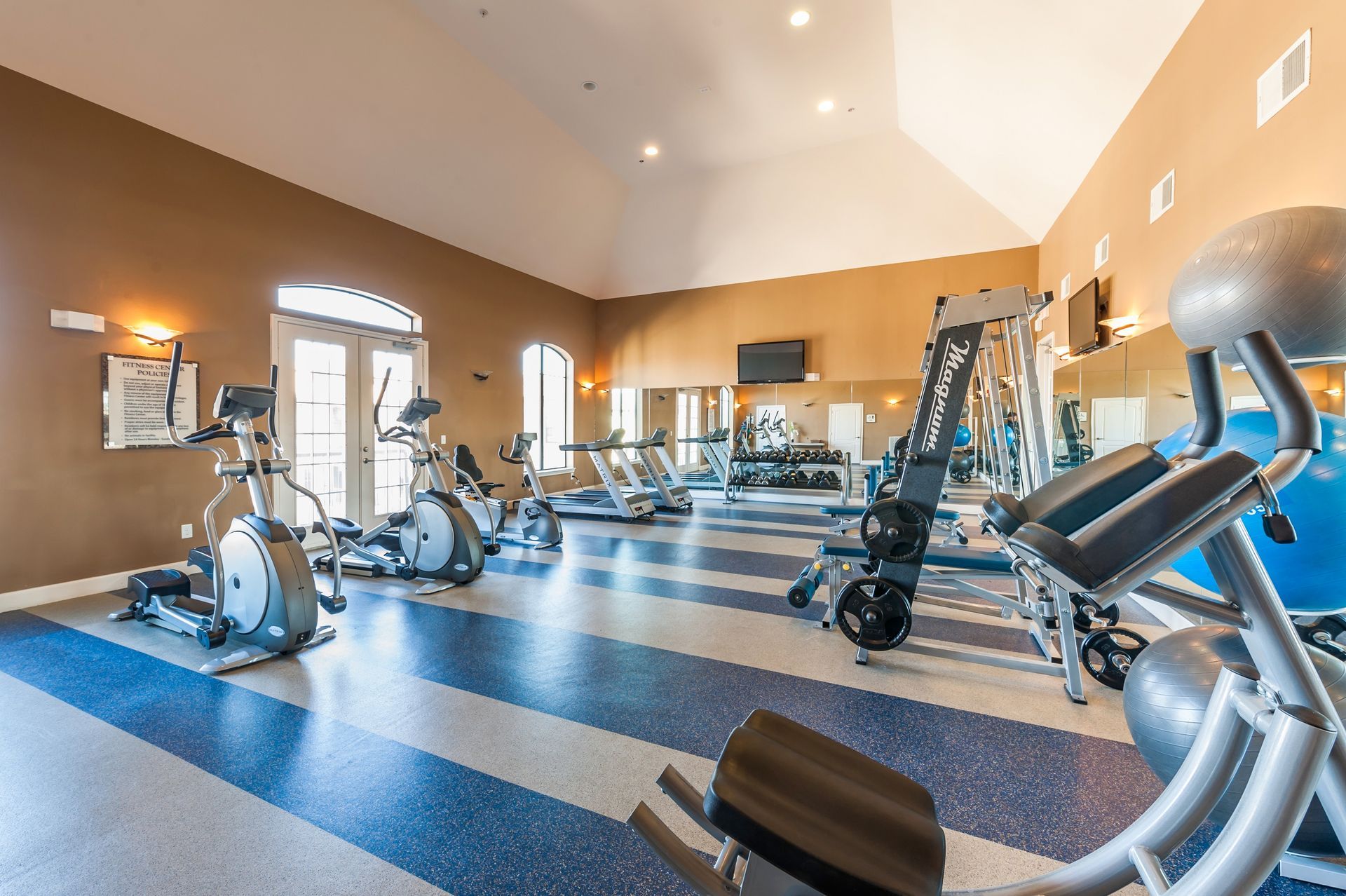 Gym interior with various exercise machines on a blue and white floor.