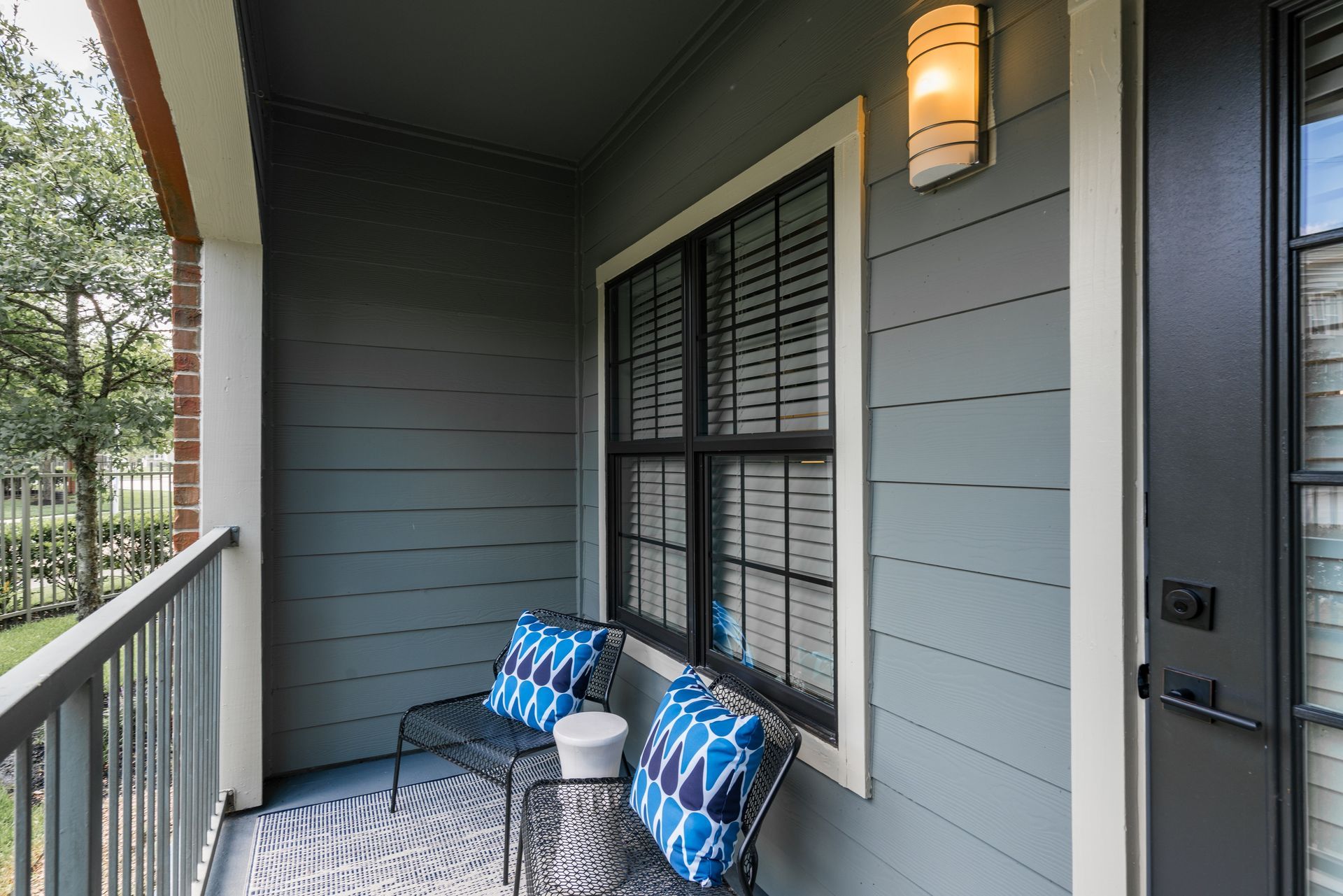Balcony with blue cushions on black chairs, a rug, and a window.