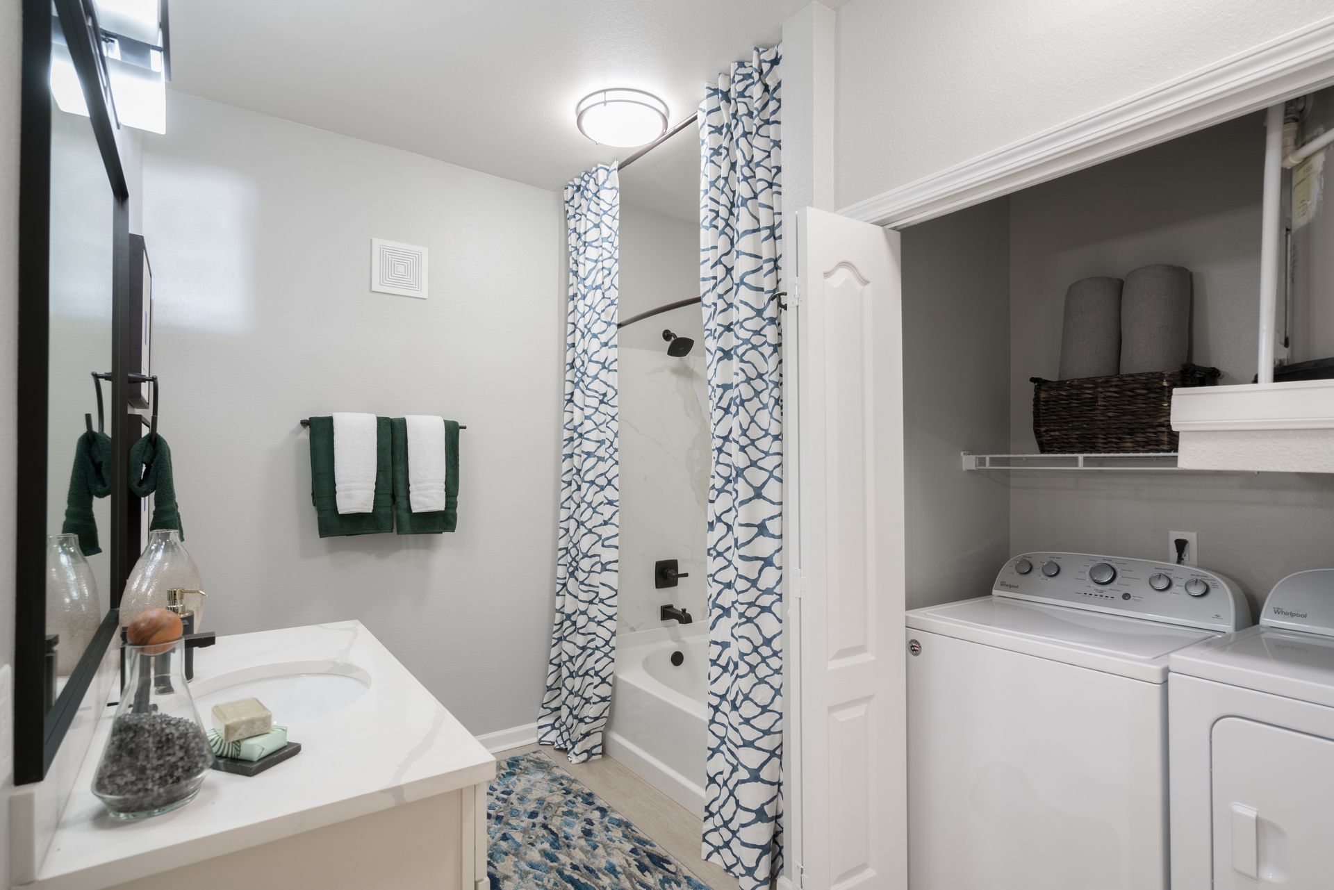 Bathroom with shower, sink, and washer/dryer. Gray walls, white cabinets, blue accents.