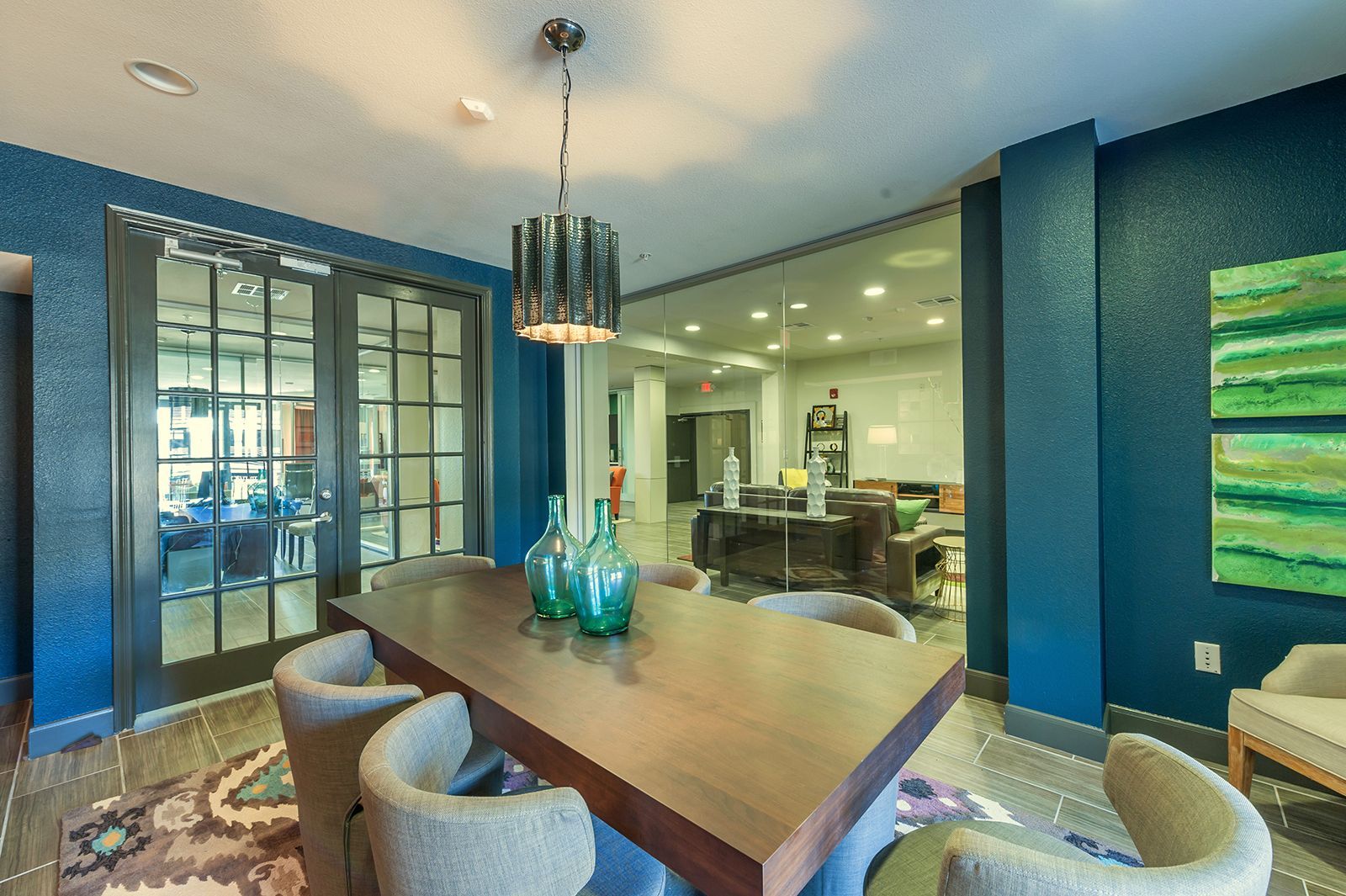 A dining area with a long wooden table, blue walls, and a view of a lounge.