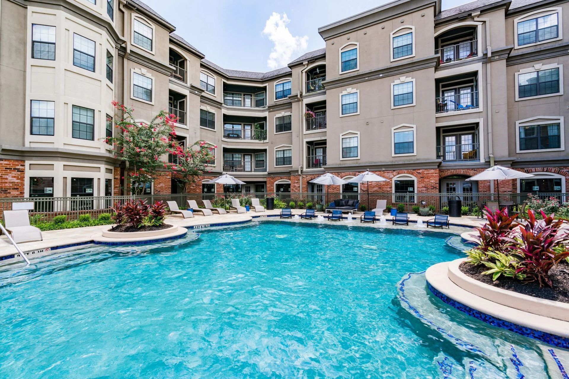 Swimming pool in courtyard of apartment complex with lounge chairs and umbrellas.