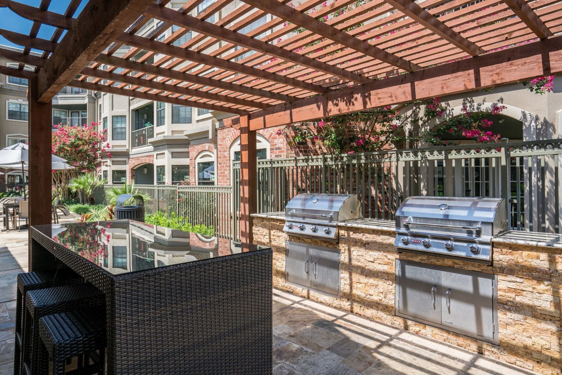 Outdoor grilling area with pergola, grills, and a bar with stools.