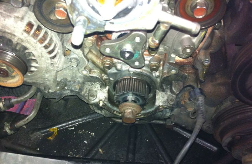 Close-up view of an exposed engine block with a central timing gear, alternator, and pulleys in a vehicle's engine bay. | Allstar Automotive