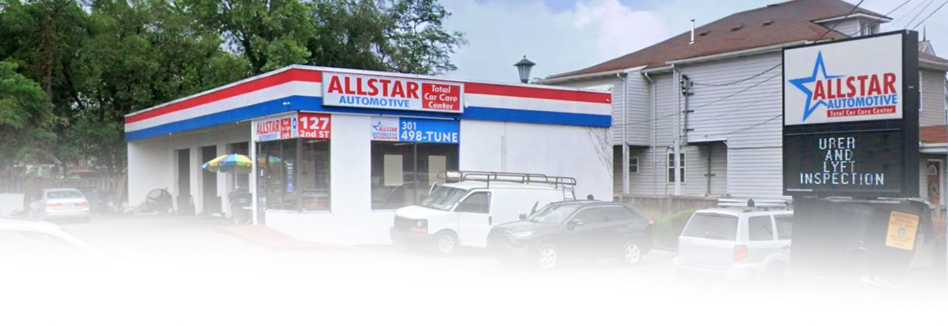 An Allstar Auto Glass shop with a red, white, and blue stripe, a white van, and a roadside sign in front of a building. | Allstar Automotive