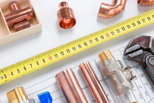 Plumbing tools, including copper pipes and fittings, a measuring tape, and a wrench, arranged on a blueprint.