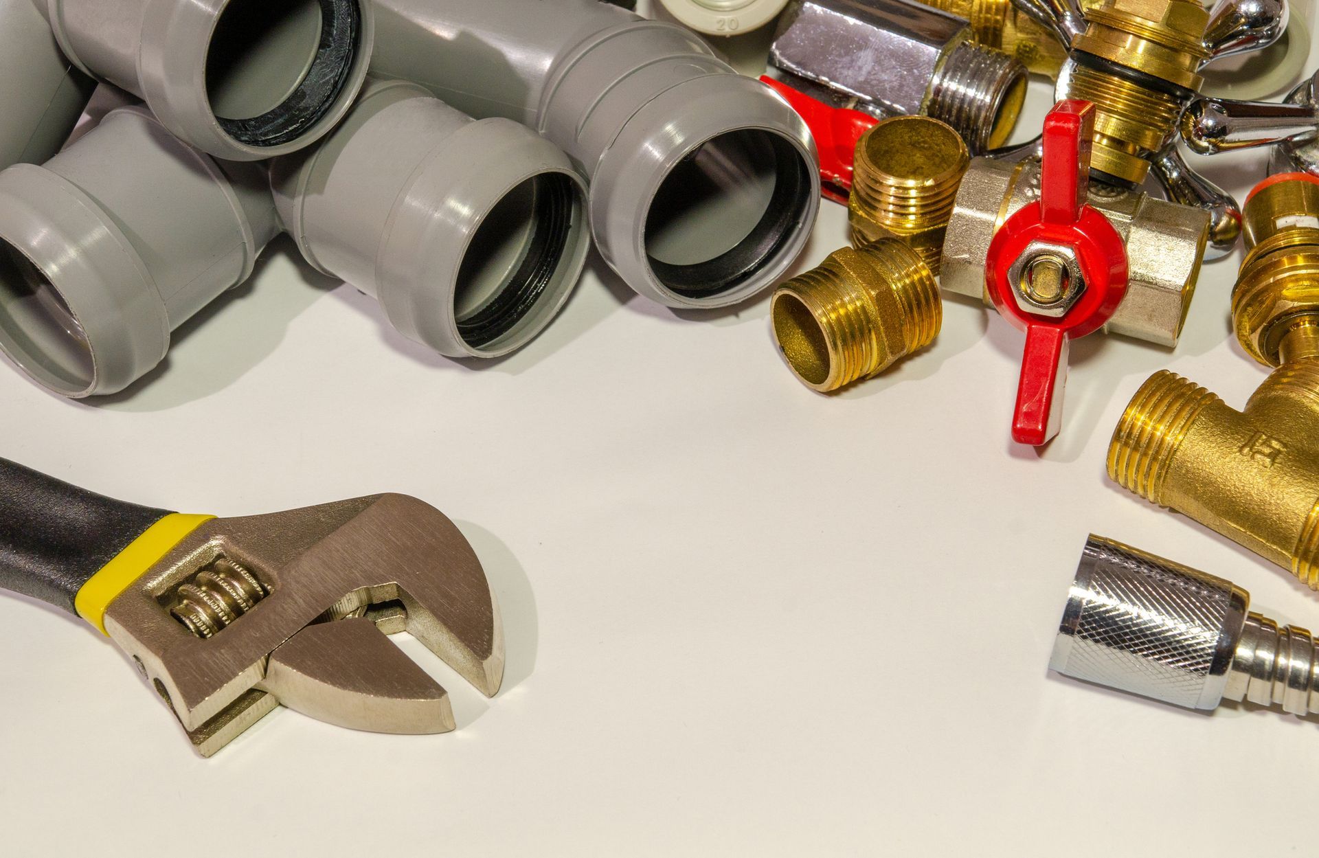 Assorted plumbing parts and an adjustable wrench are arranged on a white surface. Assorted plumbing parts and an adjustable wrench are arranged on a white surface.